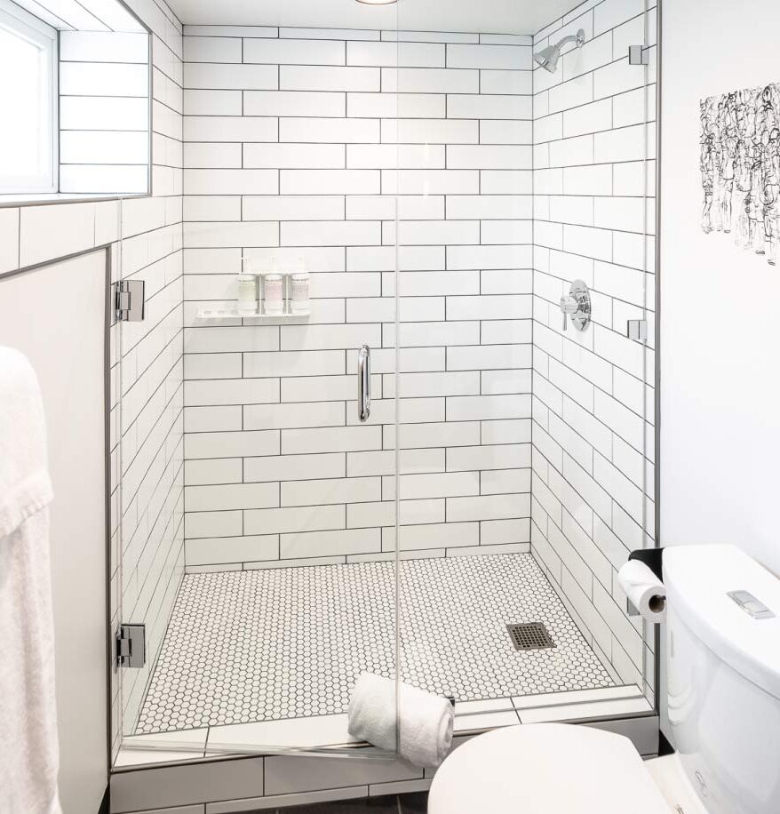 Interior of a walk in shower at our downtown Bozeman hotel. White sink and matching tile, and small vanity area