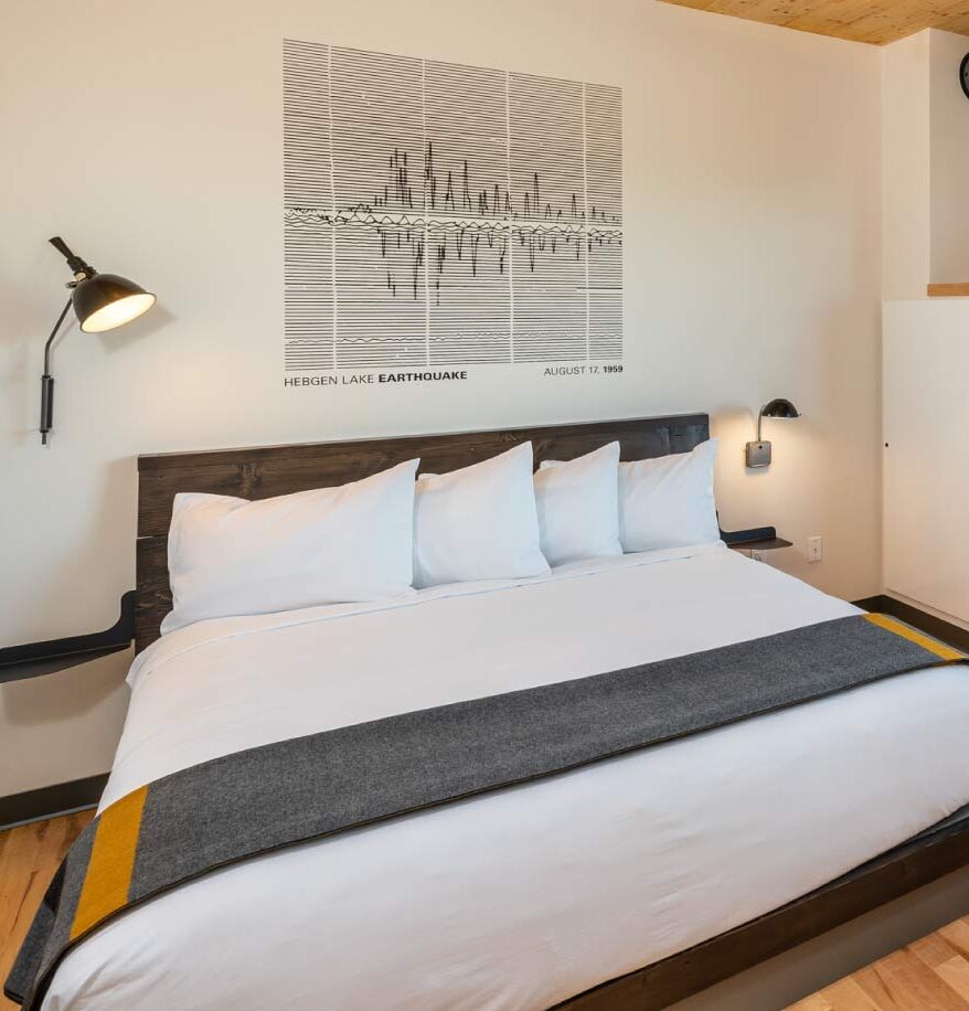 Interior view of our downtown Bozeman hotel room. Wooden flooring and ceiling, large bed, small orange chair, and a safe in room