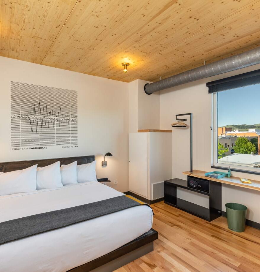 Interior view of our downtown Bozeman hotel room. Wooden flooring and ceiling, large bed, small orange chair, and a safe in room