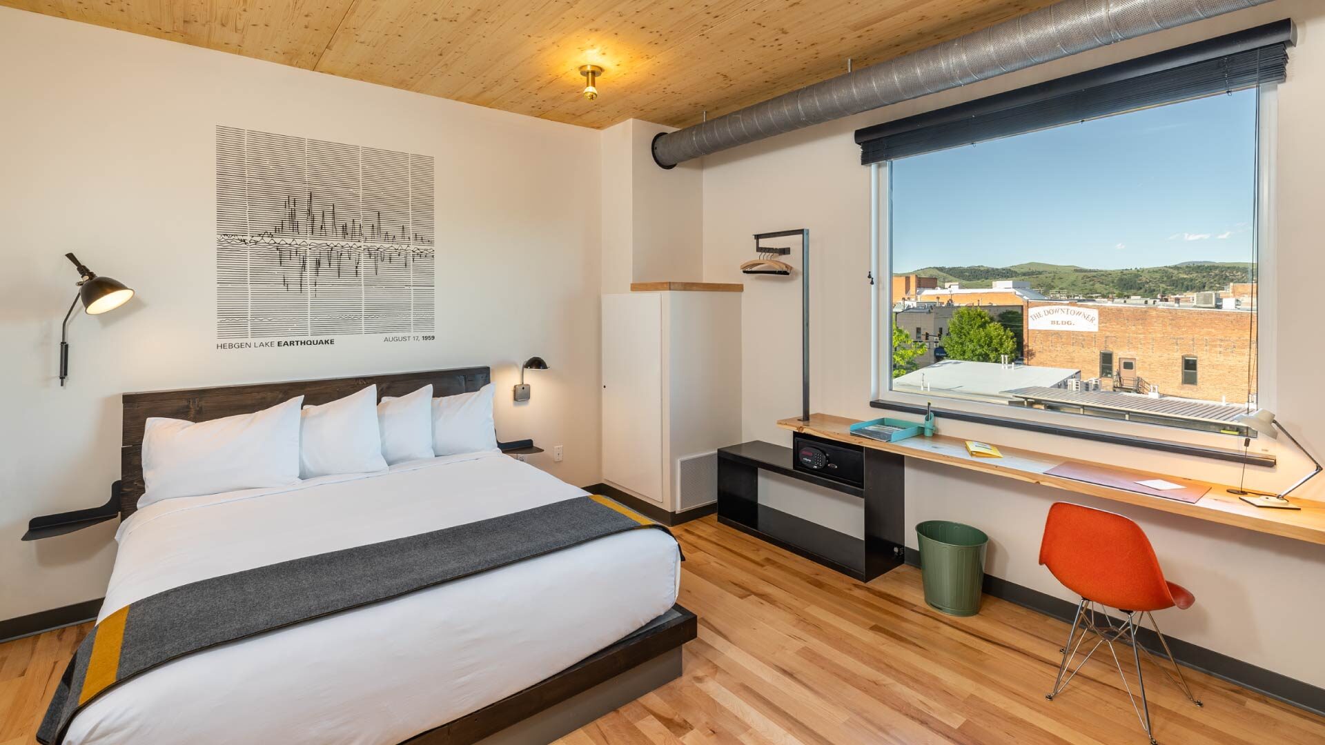 Interior view of our downtown Bozeman, Montana hotel room. Wooden flooring & ceiling, large bed, small red chair, & a safe in room