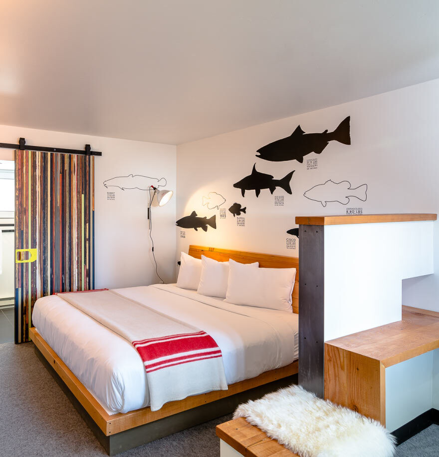 Interior view of downtown Bozeman hotel room. Wall art seen above large bed, wooden accents, and decorative bathroom door